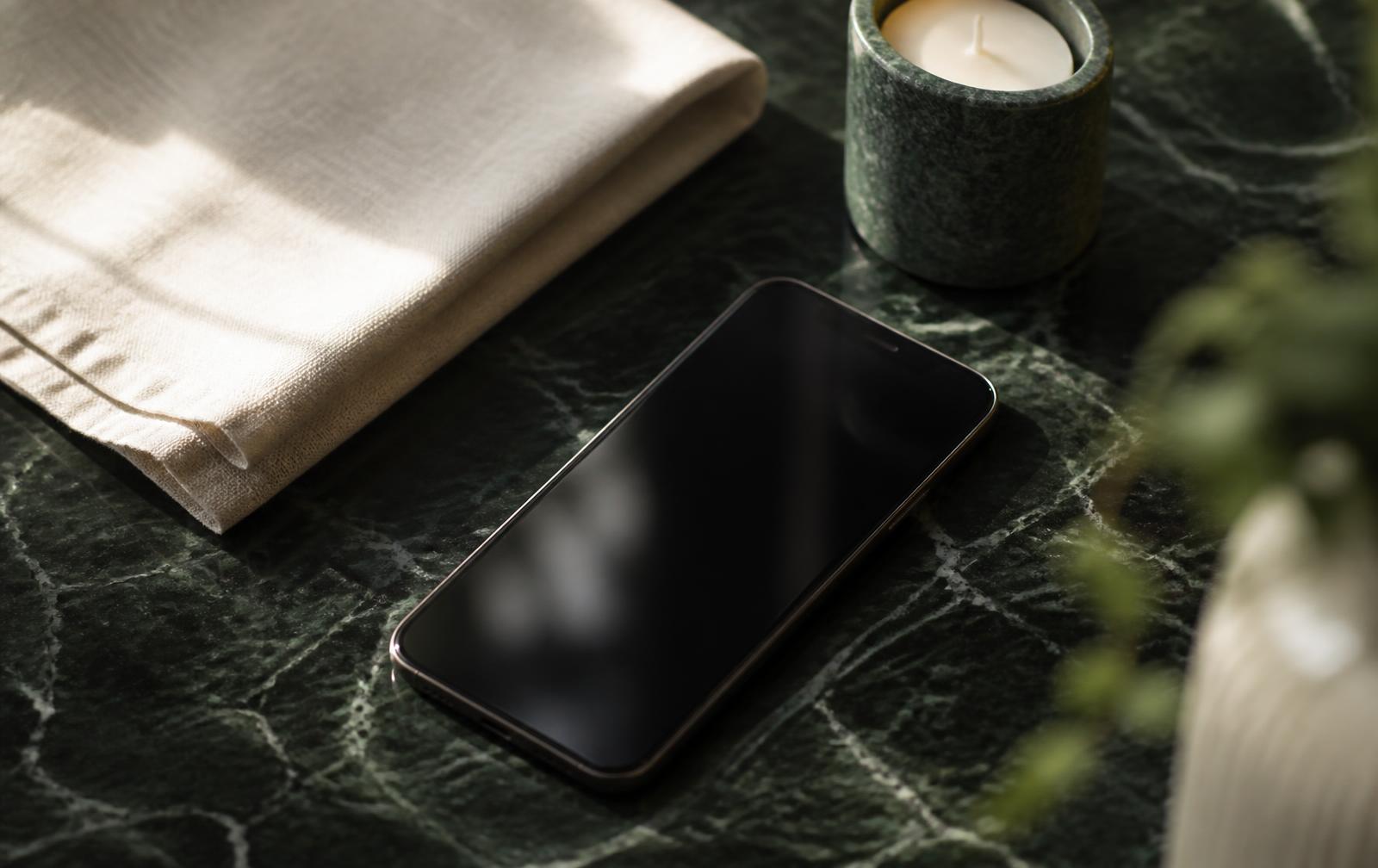 Phone on green marble beside a linen napkin and a candle